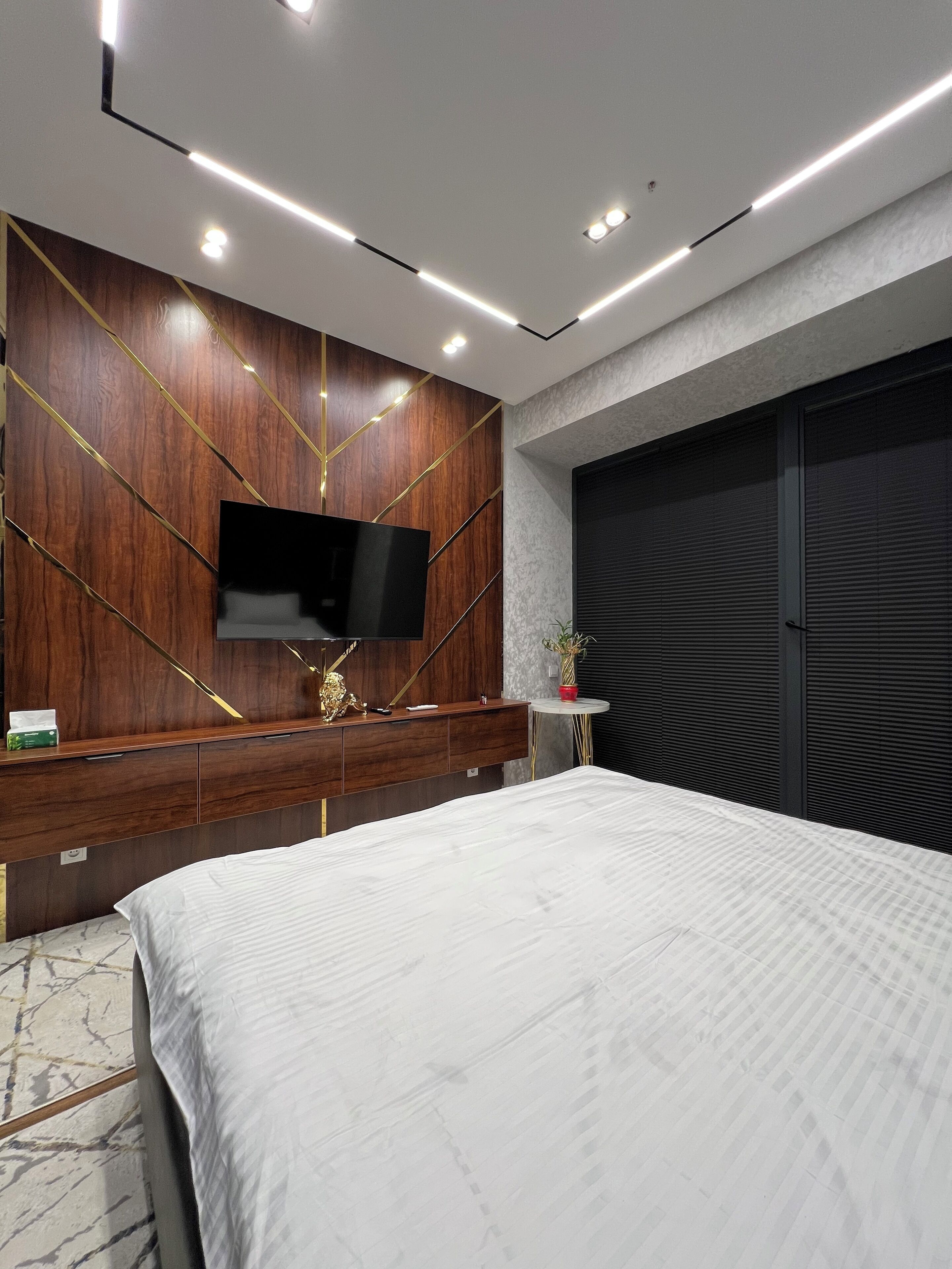 Une chambre moderne avec un grand lit, un téléviseur fixé à un mur en bois et une petite table d’appoint agrémentée d’une plante.