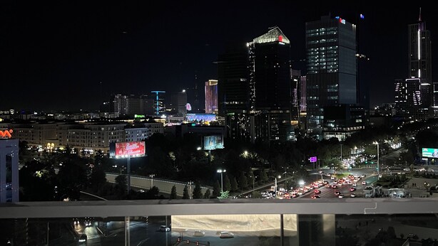 Un paisaje urbano nocturno con edificios iluminados y una calle concurrida abajo.