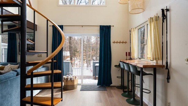 A modern interior with a spiral staircase, a dining area with bar stools, and a view through a glass door to the outdoors. - Luxe North Conway Family Retreat.Sleeps 12.Hot Tub+Game&Movie Rm+Kids Loft+Pets (Conway)