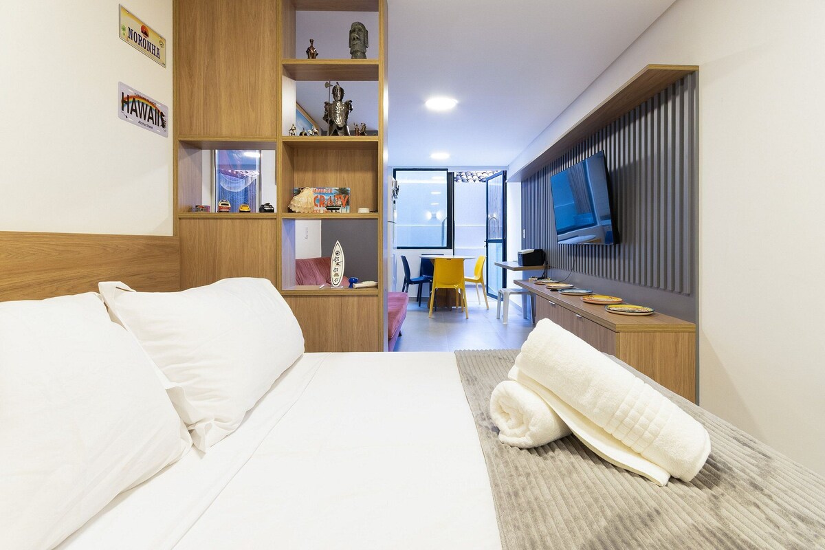 A hotel room with a bed, a desk, a TV, and a shelf with souvenirs.