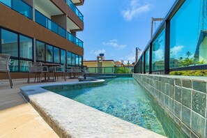 A swimming pool with lounge chairs and a view of a modern building with large windows. - Villa Del Mar - Studios in Porto de Galinhas by Carpediem (Ipojuca)