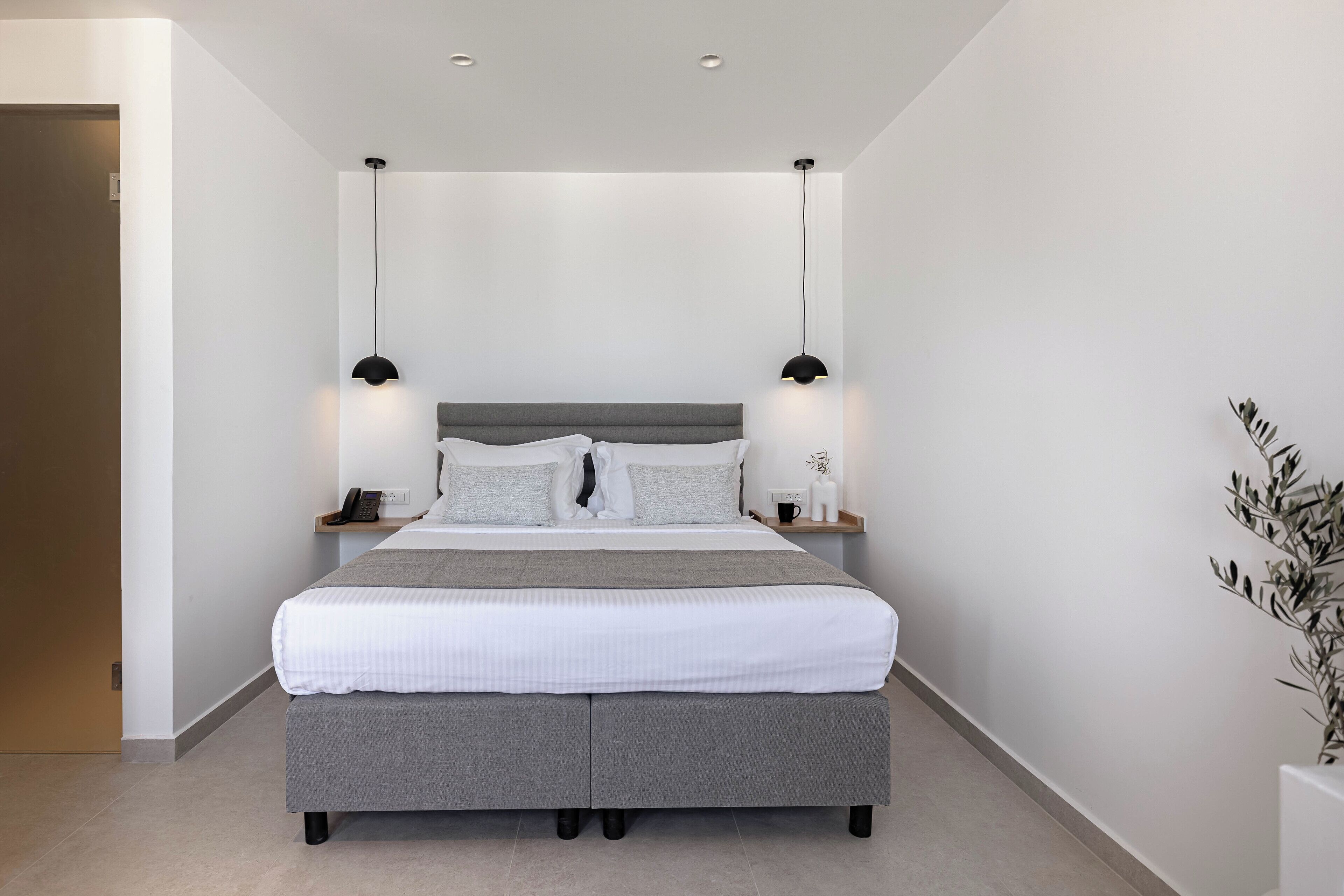 Een moderne slaapkamer met een groot bed, nachtkastjes met lampen en een kleine plant aan de rechterkant.