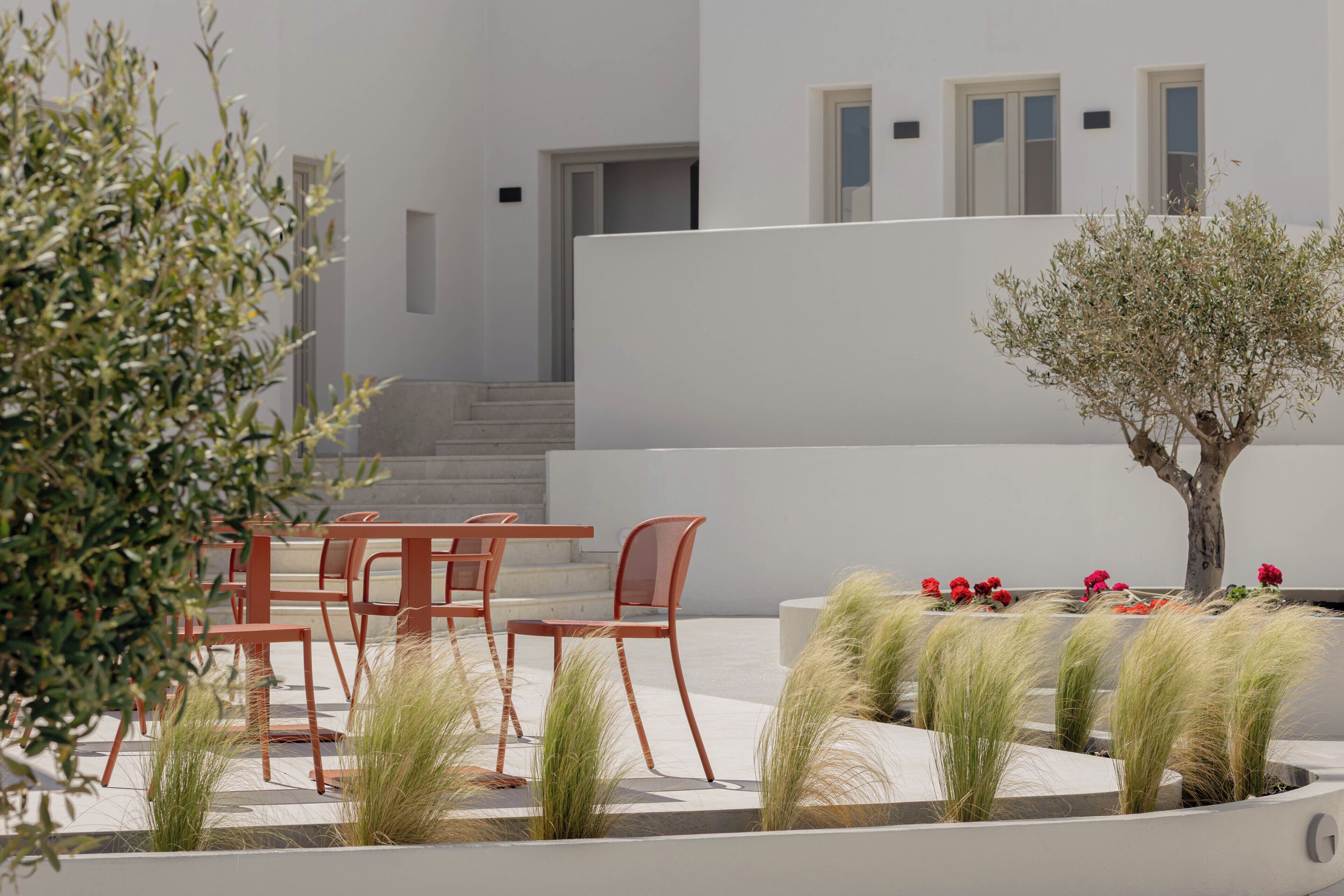 Un espace extérieur aménagé de façon moderne, avec des chaises et des tables, un petit arbre et des graminées décoratives.