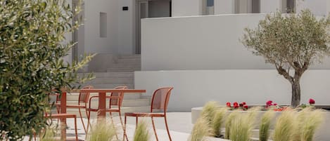 Un espace extérieur aménagé de façon moderne, avec des chaises et des tables, un petit arbre et des graminées décoratives.