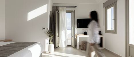 A modern hotel room with a large bed, a TV, a desk, and a view of the outdoors.