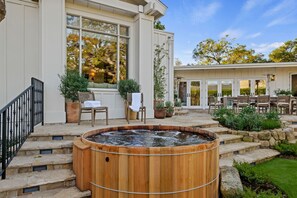 A spa area with a hot tub, outdoor seating, and a stone staircase leading to a building with large windows. - Montecito Luxury | Pickleball, Putting Green, Media Lounge, Hot tub & EV Charger (Montecito)