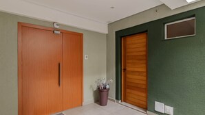 Um corredor com duas portas de madeira, um vaso com guarda-chuvas e uma parede verde com textura.
