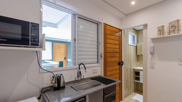 Cocina compacta con microondas, hervidor y ventana con persianas.