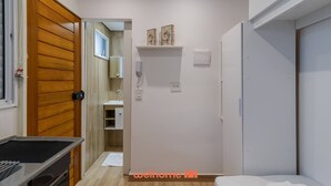 Un dormitorio pequeño con puerta de madera, mesita de noche, cama blanca y armario blanco.