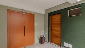 Un pasillo con dos puertas de madera, una planta en maceta con paraguas y una pared verde con textura.