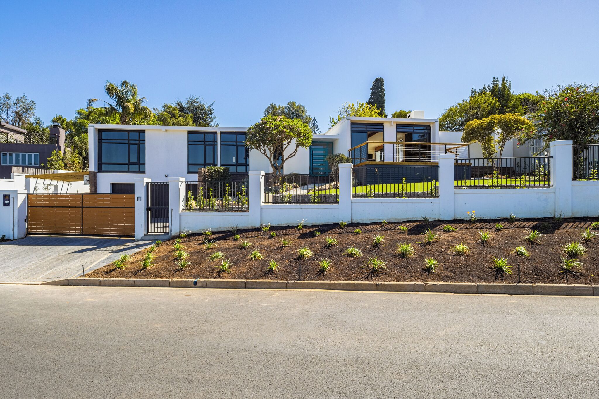 A modern two-story house with a white exterior, large windows, and a well-maintained garden.