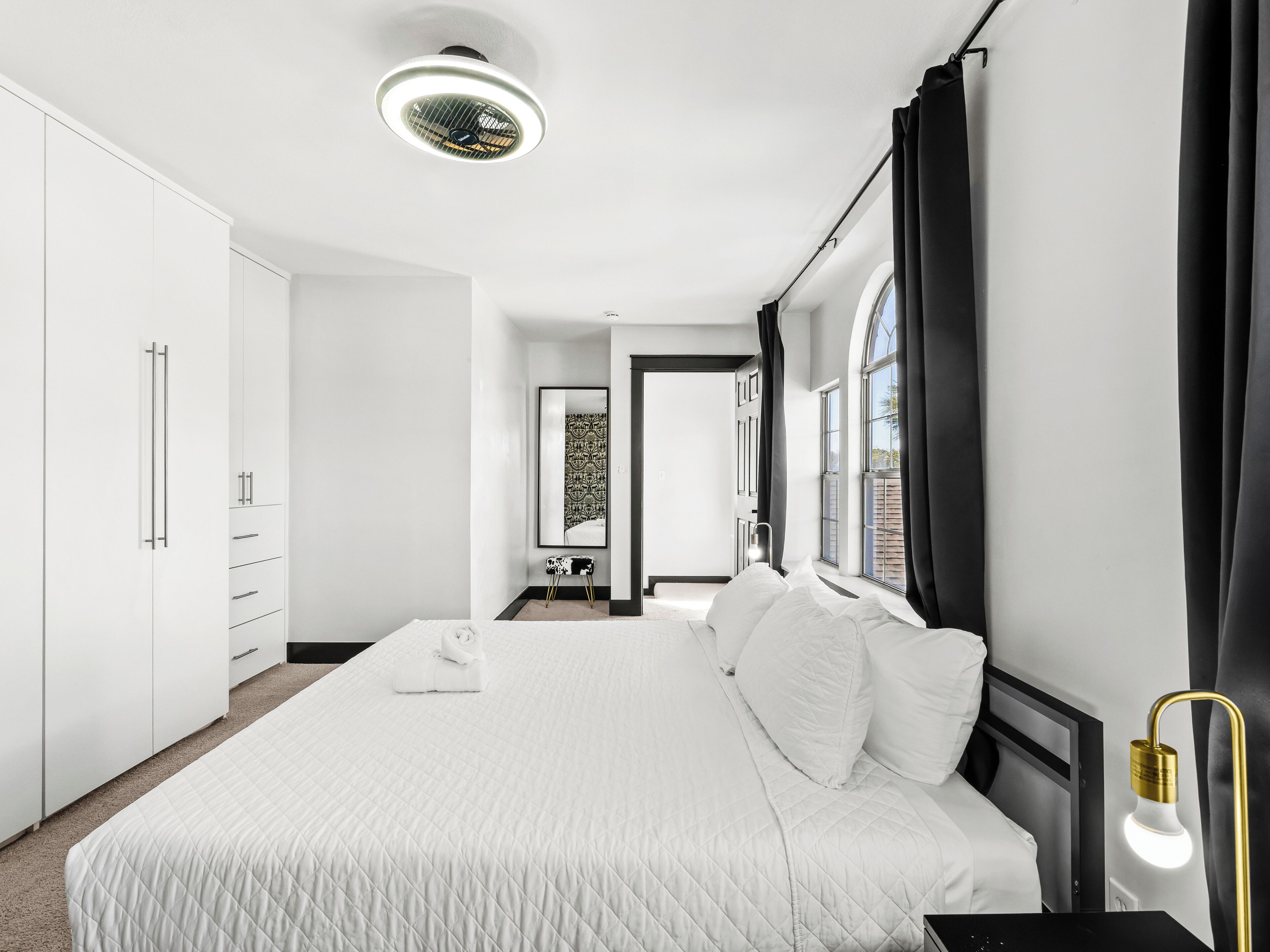 A modern bedroom with a large bed, white wardrobe, and a ceiling light fixture.