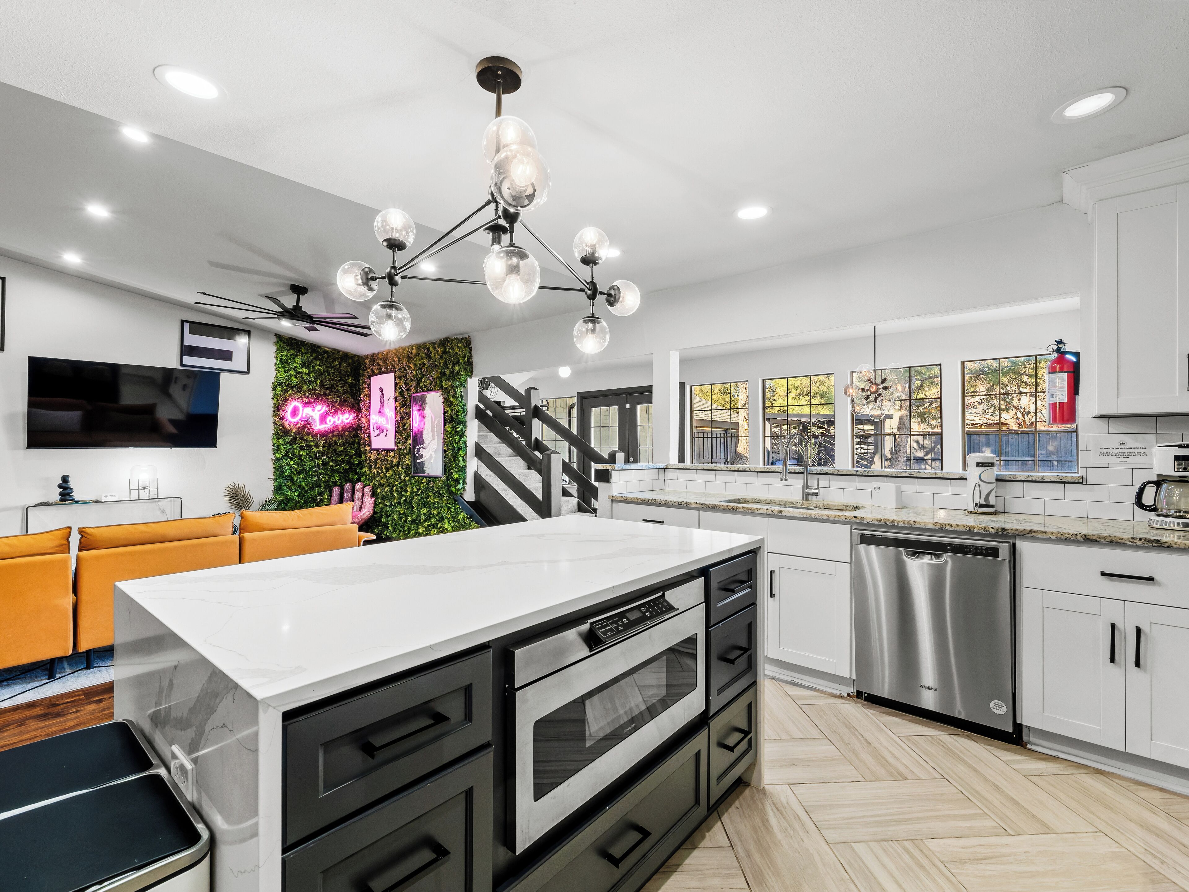 A modern kitchen with a central island, stainless steel appliances, and a green wall with a neon sign.