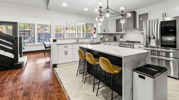 A modern kitchen with a central island, bar stools, stainless steel appliances, and large windows. - Stunning Carrolton Castle with 4 Bedrooms + Pool + Media Room (Carrollton)