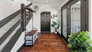 A hallway with a wooden floor, a staircase with a metal railing, a door with glass panels, and a potted plant. - Stunning Carrolton Castle with 4 Bedrooms + Pool + Media Room (Carrollton)