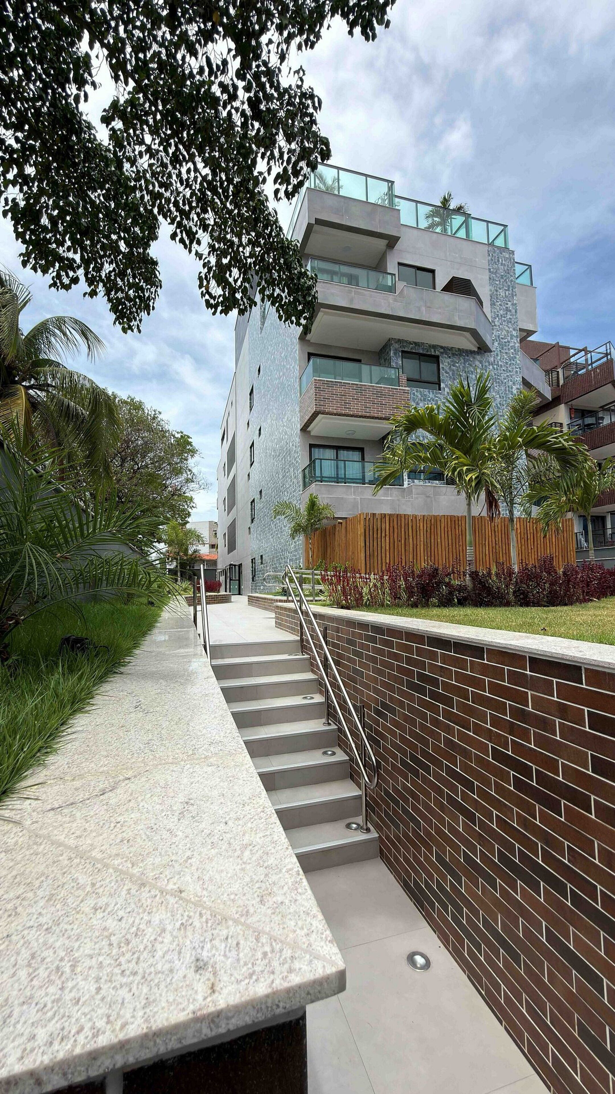 Un edificio moderno con una escalera que conduce a una entrada con puerta, rodeado de follaje y palmeras.