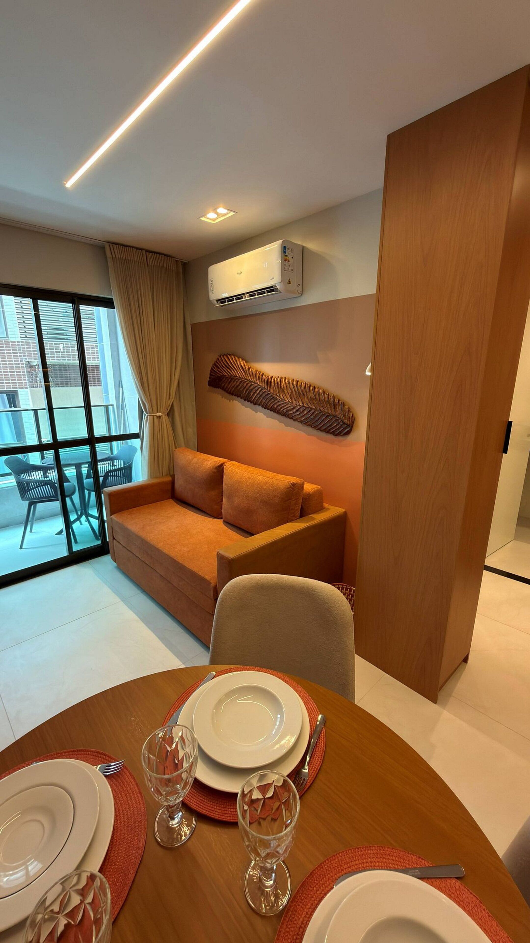 A modern living room with a sofa, a dining table set for four, and an air conditioning unit on the wall.