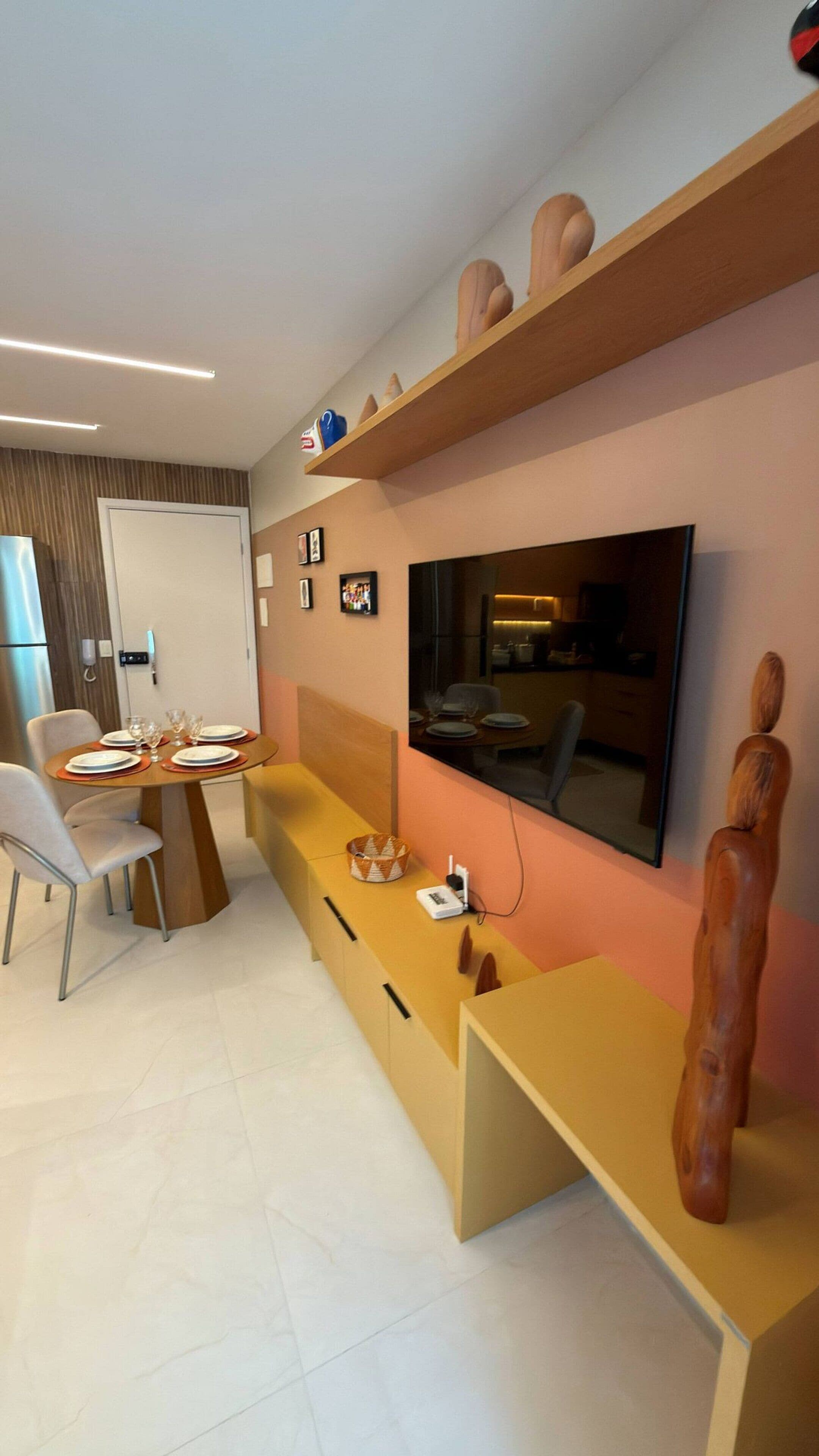 A modern living room with a dining area, a flat-screen TV mounted on the wall, and a wooden sculpture.