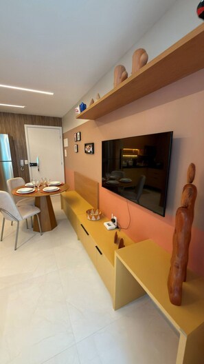 A modern living room with a dining area, a flat-screen TV mounted on the wall, and a wooden sculpture. - Porto Ibiza (Ipojuca)