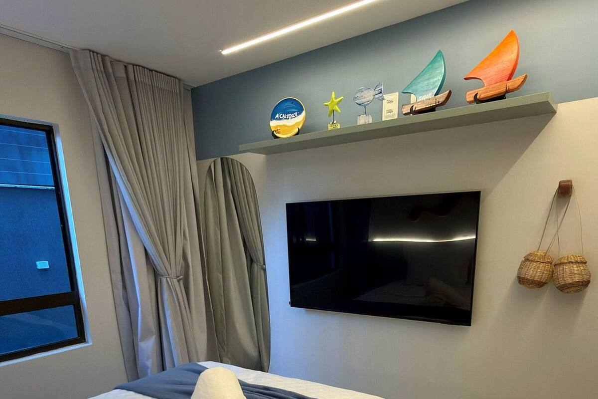 Una habitación de hotel moderna con una cama, un televisor de pantalla plana, una estantería con adornos y una ventana con cortinas.