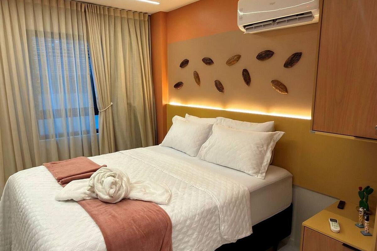 Habitación de hotel con cama, mesita de noche con teléfono, equipo de aire acondicionado y ventana con cortinas.