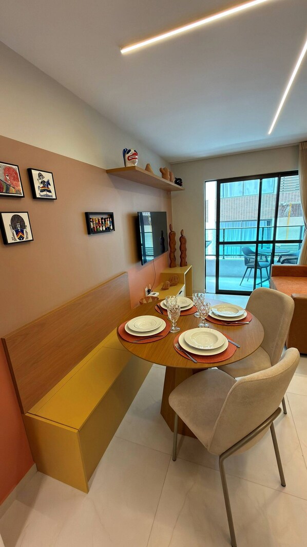 Un comedor con una mesa de madera dispuesta para cuatro, un banco y un televisor montado en la pared.