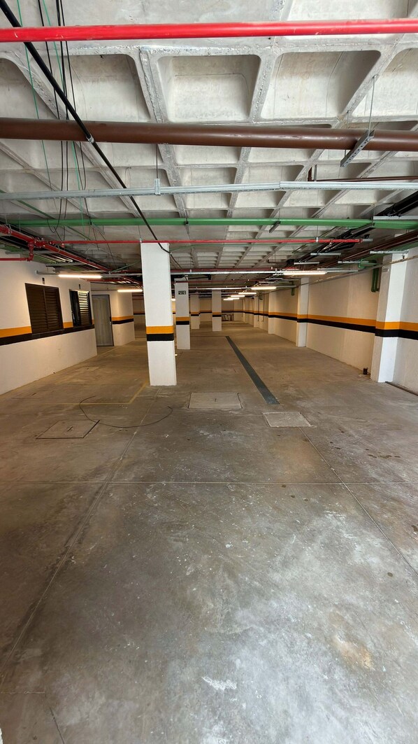 A large, empty parking garage with concrete floors and pillars, and visible electrical conduits on the ceiling.