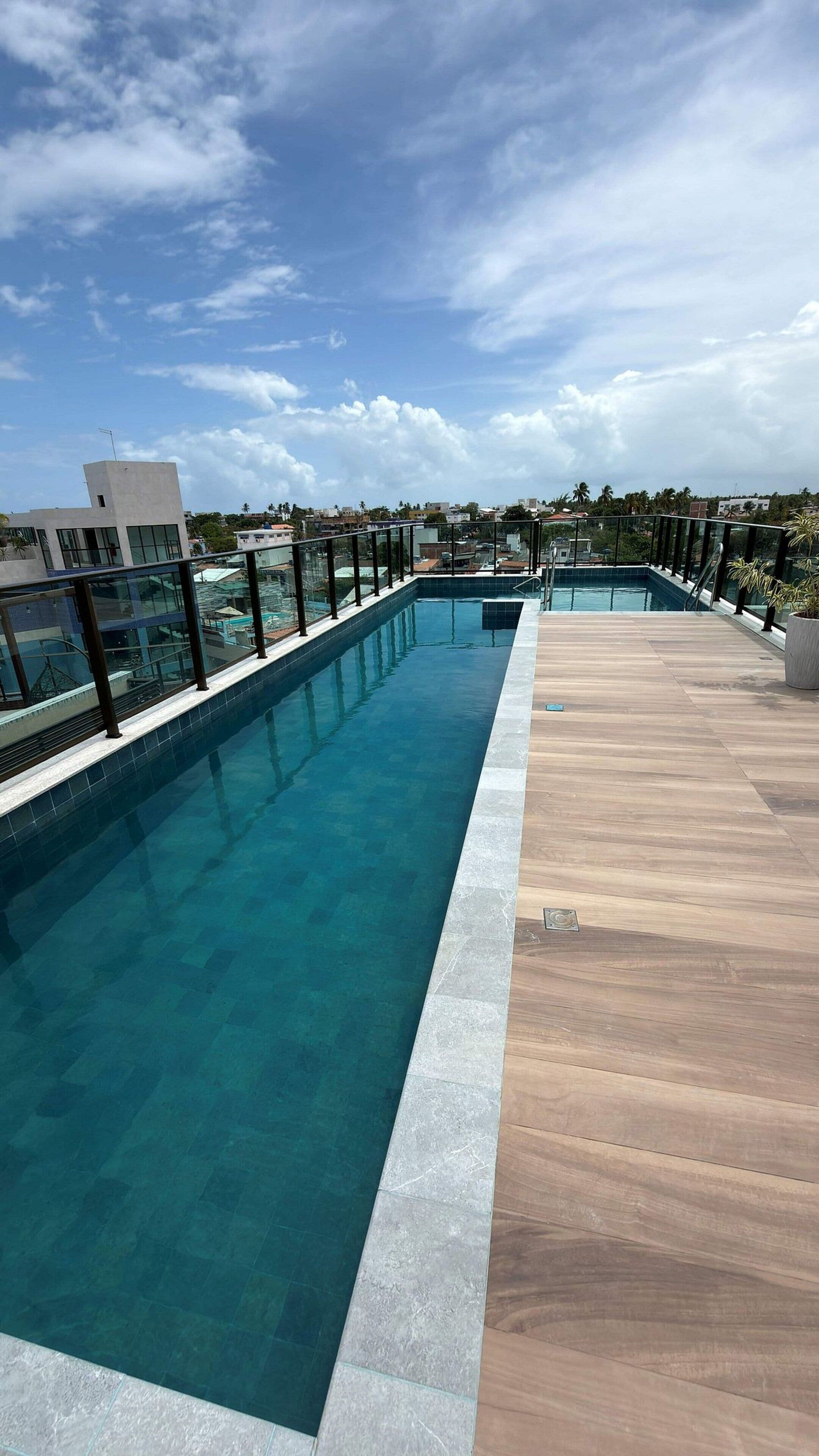 Une piscine sur le toit, avec une eau d’un bleu cristallin, entourée d’une terrasse en bois et de rampes de protection en verre.