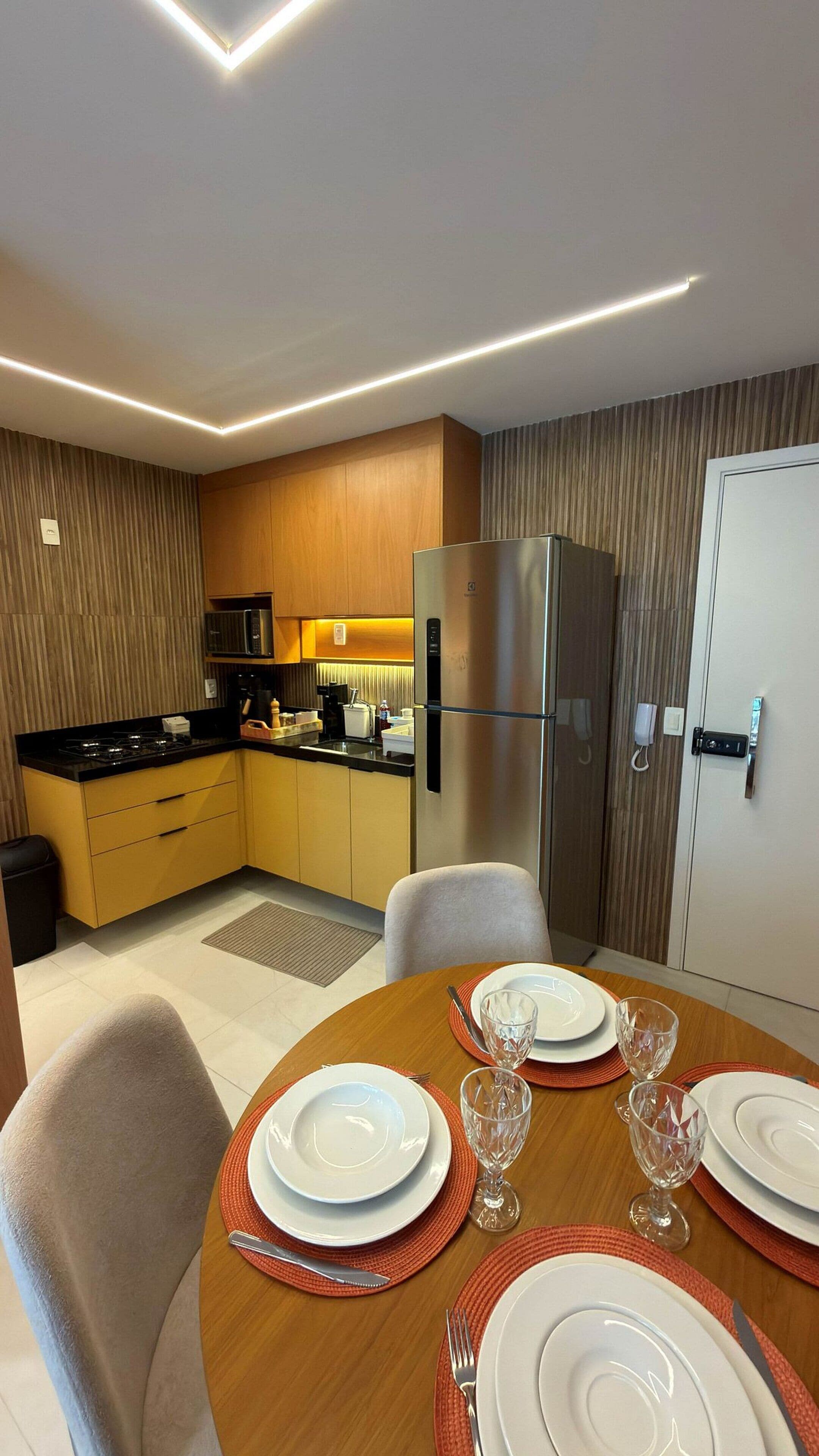 A modern kitchen with a refrigerator, microwave, and stove. There is a dining table set with plates and glasses.