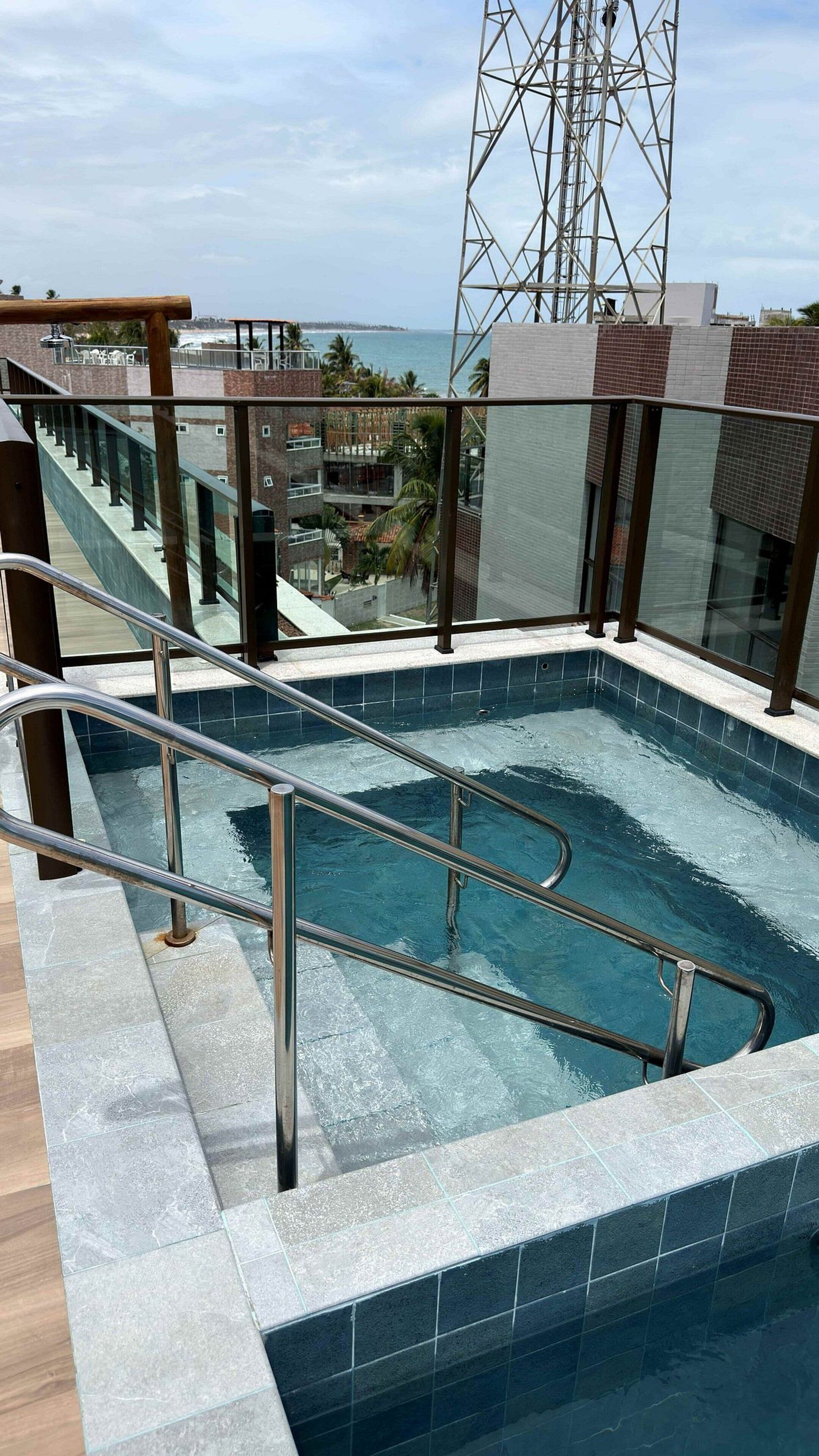 A rooftop swimming pool with metal railings, a view of the ocean, and a tall communication tower in the background.
