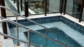 A rooftop swimming pool with metal railings, a view of the ocean, and a tall communication tower in the background.