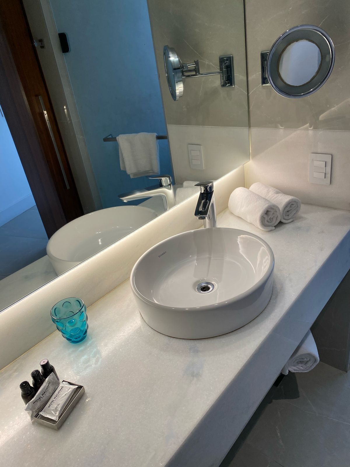 A modern bathroom with a round sink, a large mirror, and a towel rack.