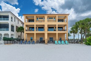 Een hotel met meerdere verdiepingen, balkons, een zandstrand ervoor en palmbomen.