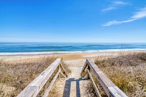 A wooden boardwalk leading to a beach with clear blue skies. - Oceanfront condo in Duck with community pool! (Duck)