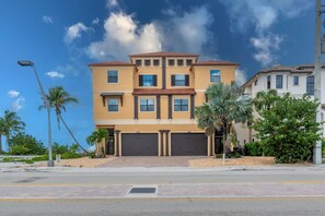 A multi-story residential building with a symmetrical facade, large garage doors, and a well-maintained front yard with palm trees. - 🌴Luxury Beachfront | Private Pool | Elevator | Stunning Views | Blue Paradise🌴 (Fort Myers Beach)