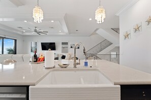 A modern kitchen with a central island, a built-in sink, pendant lights, and a staircase leading to an upper level. - 🌴Luxury Beachfront | Private Pool | Elevator | Stunning Views | Blue Paradise🌴 (Fort Myers Beach)
