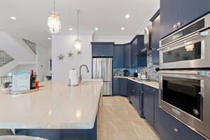 A modern kitchen with a large island, stainless steel appliances, and decorative star wall art. - 🌴Luxury Beachfront | Private Pool | Elevator | Stunning Views | Blue Paradise🌴 (Fort Myers Beach)