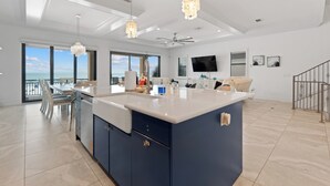 Une cuisine moderne dotée d’un grand îlot central, de luminaires suspendus et offrant une vue sur l’extérieur.