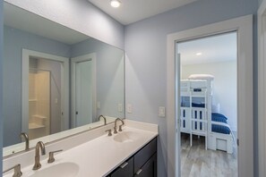 A bathroom with a double sink, a large mirror, and a bunk bed in the adjacent room. - Gorgeous semi-oceanfront home on the 4x4 beaches w/ swim spa & ocean views! (Carova)
