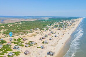 An aerial view of a coastal area with houses along the beach, a clear sky, and a calm sea. - Gorgeous semi-oceanfront home on the 4x4 beaches w/ swim spa & ocean views! (Carova)