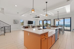 A spacious kitchen with a large island, pendant lighting, and a view of the ocean.
