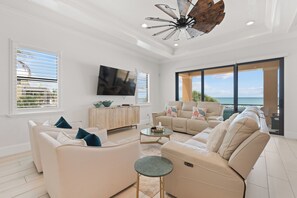 A spacious living room with a large TV, multiple seating areas, and a view of the ocean. - 🌅Gulf Front Stunner | Private Pool + Spa | Elevator | Sunset Siesta🌅 (Fort Myers Beach)
