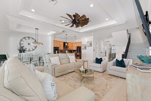 A spacious living room with a high ceiling, a large clock, and a modern ceiling fan.