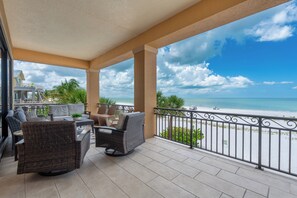 A covered outdoor seating area with wicker furniture, a view of the beach, and a clear sky. - 🌅Gulf Front Stunner | Private Pool + Spa | Elevator | Sunset Siesta🌅 (Fort Myers Beach)