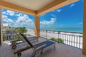 A balcony with two lounge chairs, a small table, and a wheelbarrow. - 🌅Gulf Front Stunner | Private Pool + Spa | Elevator | Sunset Siesta🌅 (Fort Myers Beach)