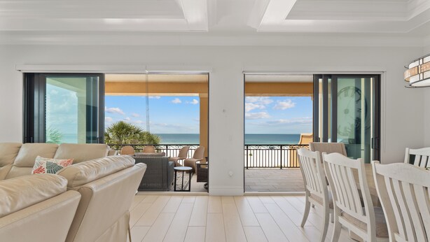 Ein großzügiger Wohnbereich mit Balkon und Meerblick, ausgestattet mit einer Couch, Sesseln und einem Esstisch.