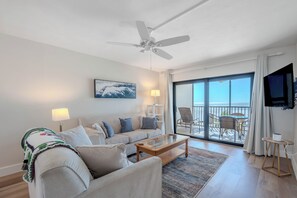 A modern living room with a sofa, coffee table, and a balcony with outdoor furniture. - 🌅Gulf Front | Awesome Amenities | Carlos Pointe #515 - The Pelican Pad🌅 (Fort Myers Beach)