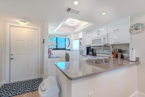 A modern kitchen with white cabinets, a granite countertop, a stainless steel sink, and a microwave. - 🌅Gulf Front | Awesome Amenities | Carlos Pointe #515 - The Pelican Pad🌅 (Fort Myers Beach)
