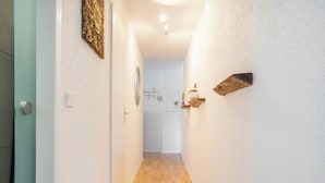 Un corridoio stretto con pavimento in legno, pareti bianche e una porta a sinistra.