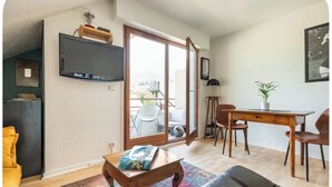 Un soggiorno con divano, tavolino, televisore a parete, tavolo da pranzo e sedie, e una porta scorrevole in vetro che dà su uno spazio esterno.